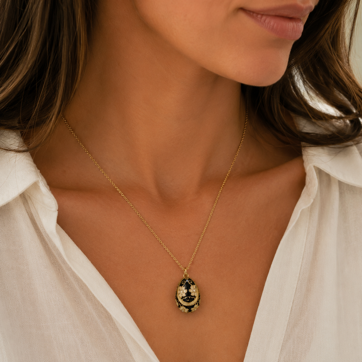 A close-up of a woman wearing a delicate gold chain necklace with an oval pendant featuring a black and gold crescent moon design.