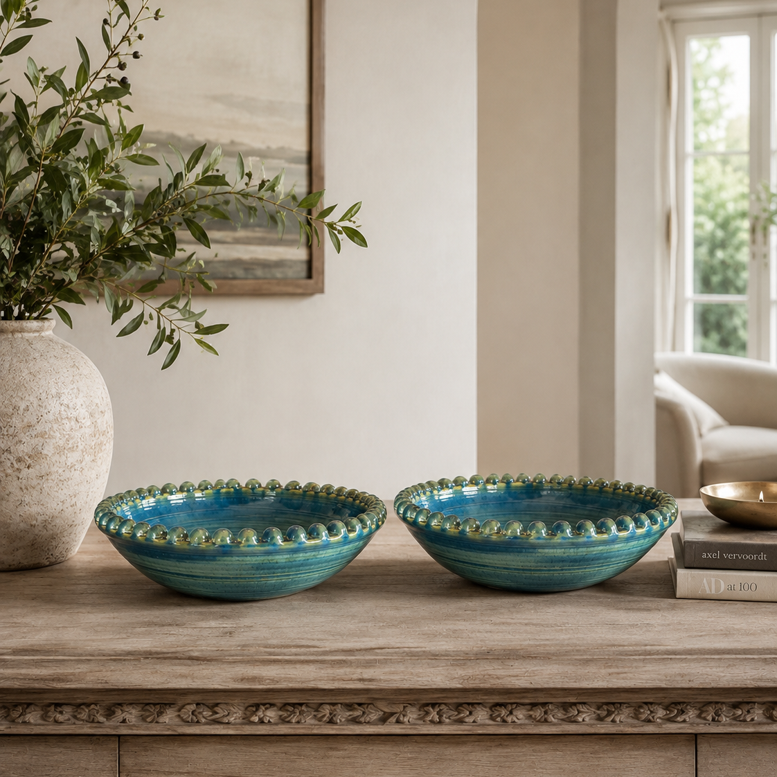 Two teal ceramic bowls with scalloped rims displayed on a wooden console table in a styled interior setting.