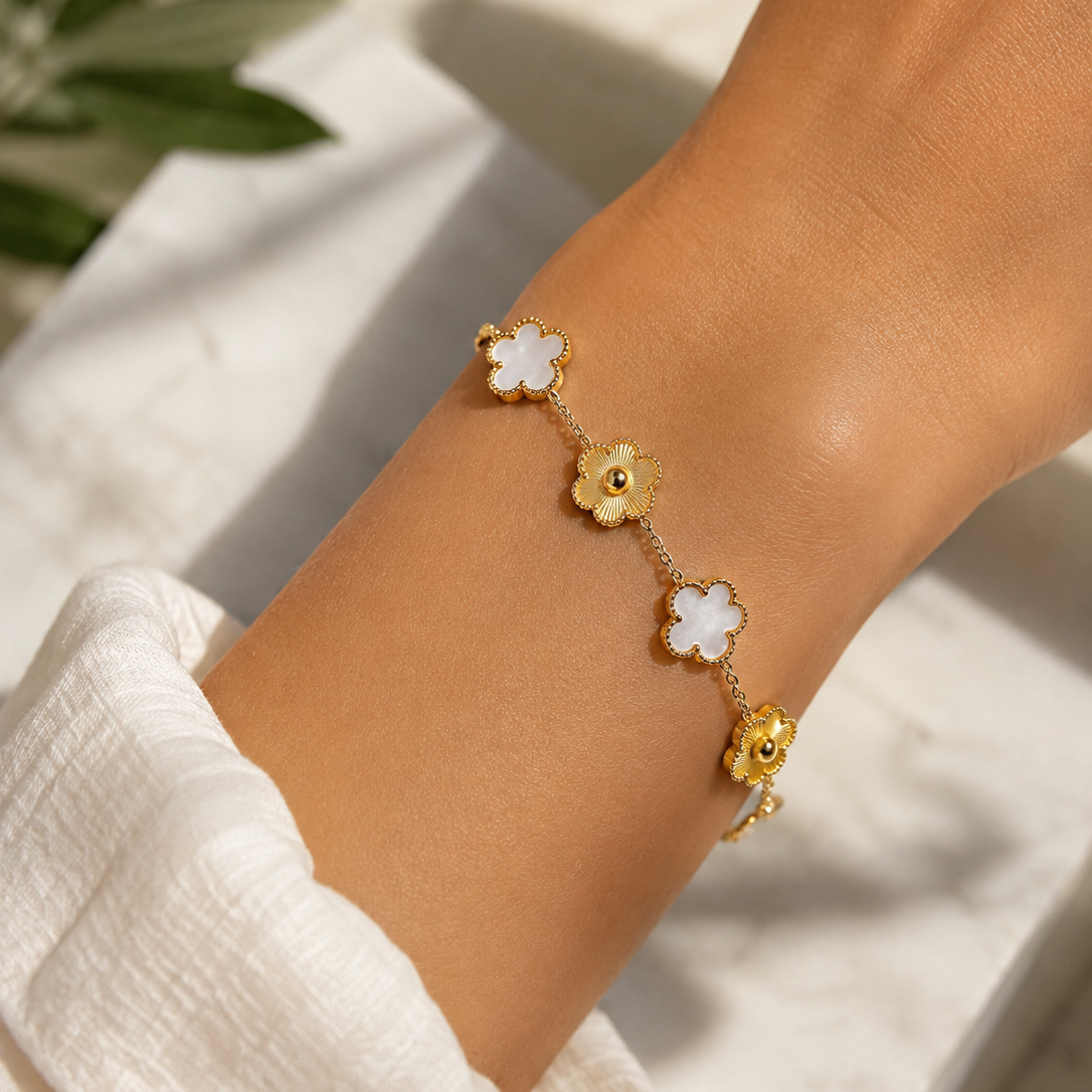 A delicate gold chain bracelet with alternating white flower and yellow flower charms, shown worn on a person's wrist.
