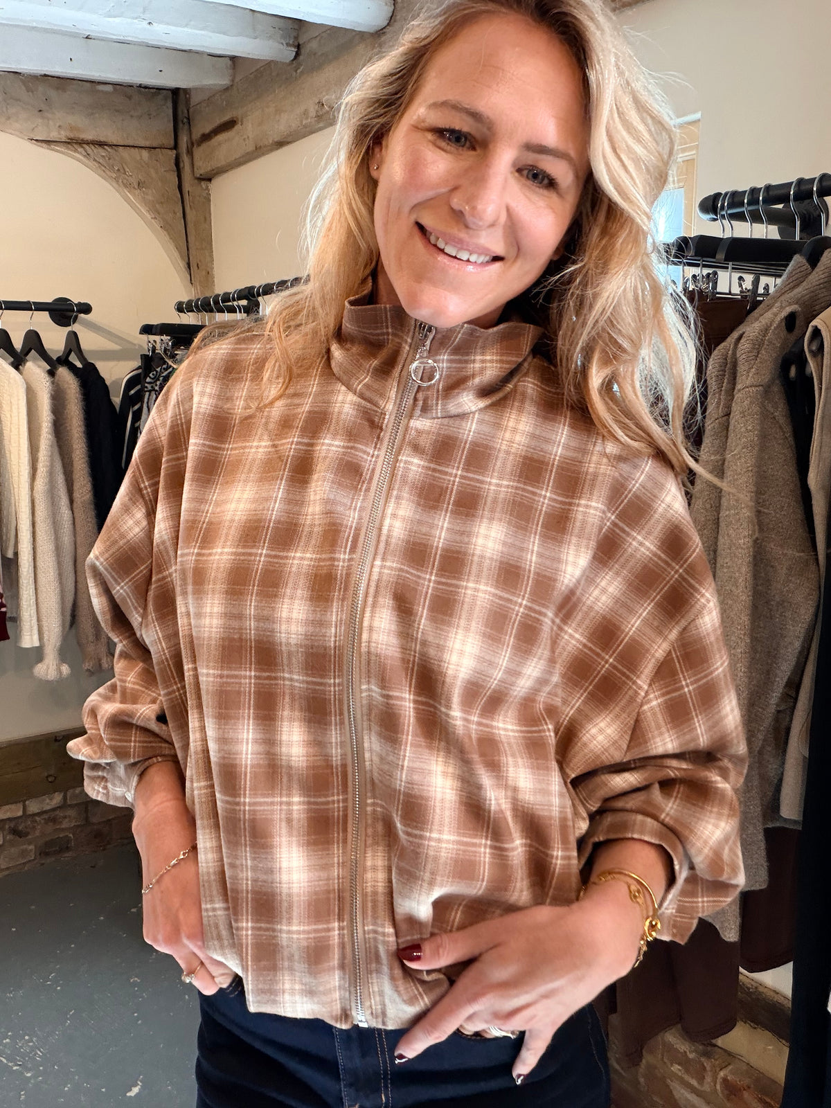 A woman wearing a brown and beige plaid zip-up jacket in a clothing boutique setting.