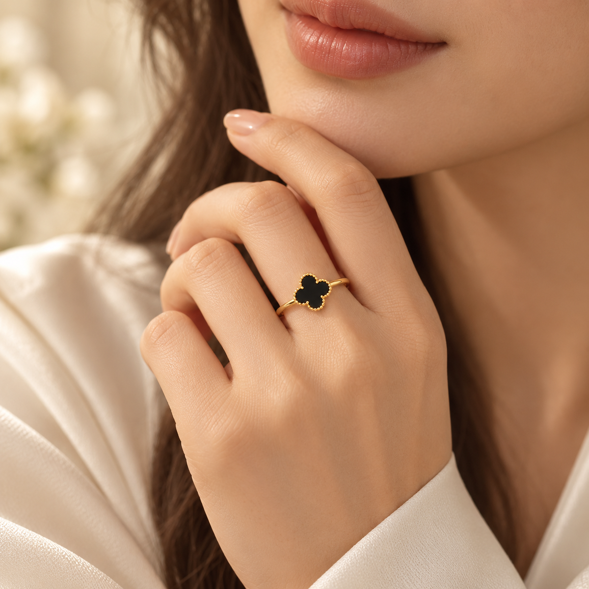 A close-up lifestyle shot of a model wearing a delicate gold ring with a black four-petal clover design on her finger.