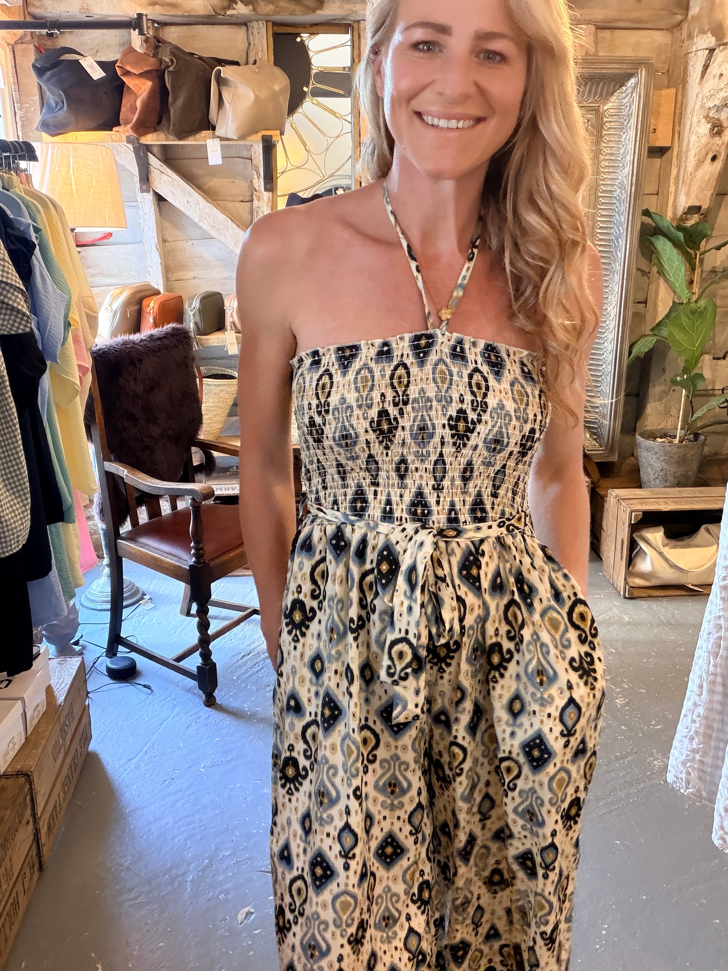 A woman wearing a strapless halter-neck dress with a black, beige, and white geometric ikat pattern, standing inside a rustic shop.