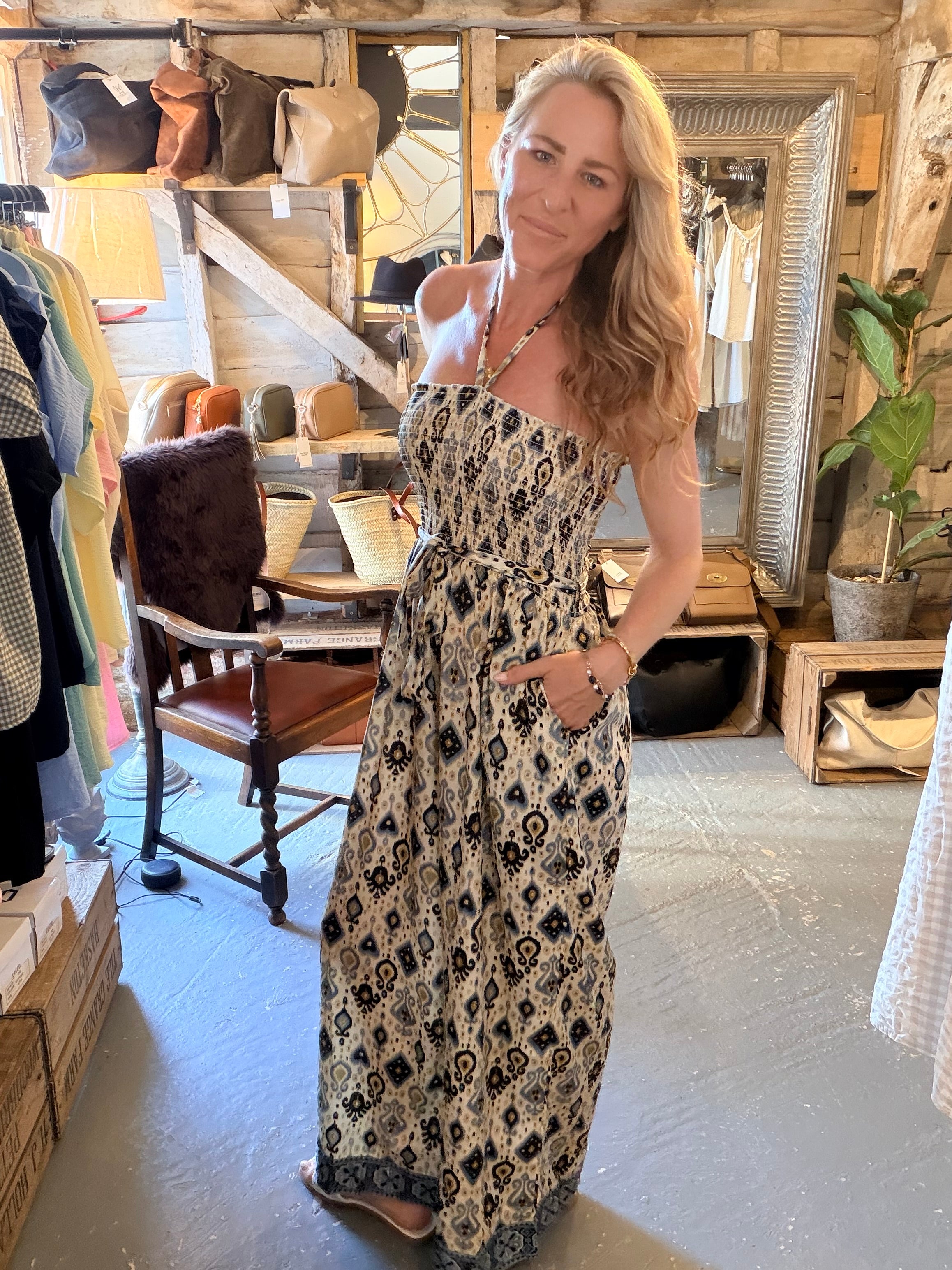 A woman modeling a strapless maxi dress with a black and beige bohemian pattern in a rustic clothing boutique.
