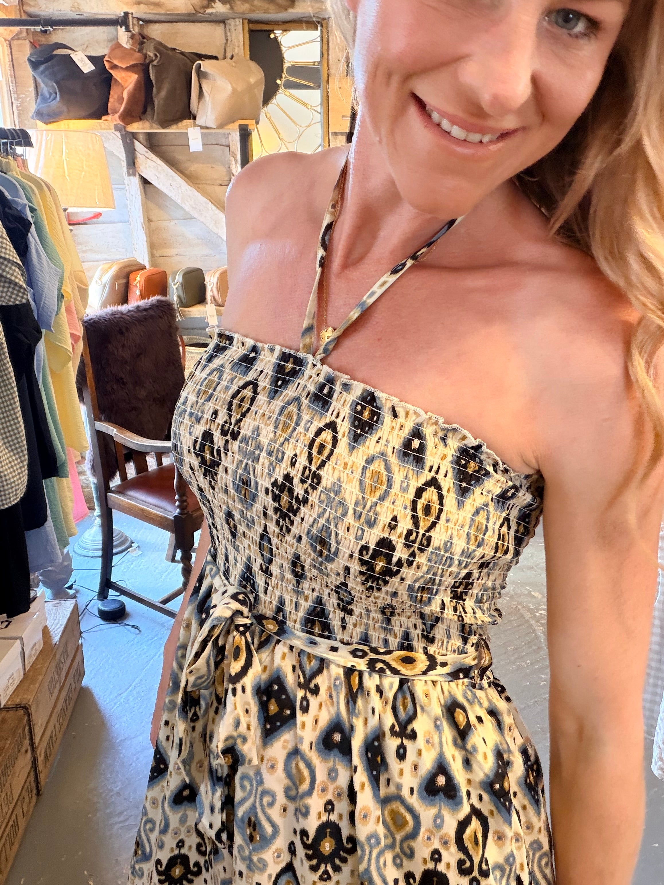 A woman wearing a strapless halter dress with a beige, black, and brown ikat pattern, photographed in a boutique setting.