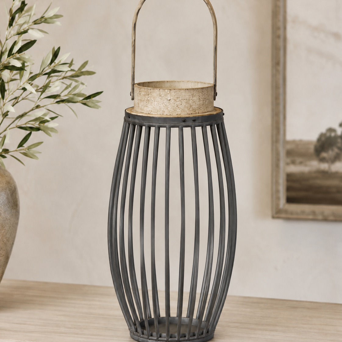 A tall black metal lantern with vertical slats and a curved top handle, styled on a light wood console table in a warm interior setting.