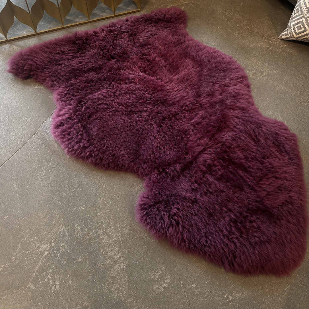 A deep purple shaggy sheepskin-style rug laid out on a gray concrete floor in a styled interior setting.
