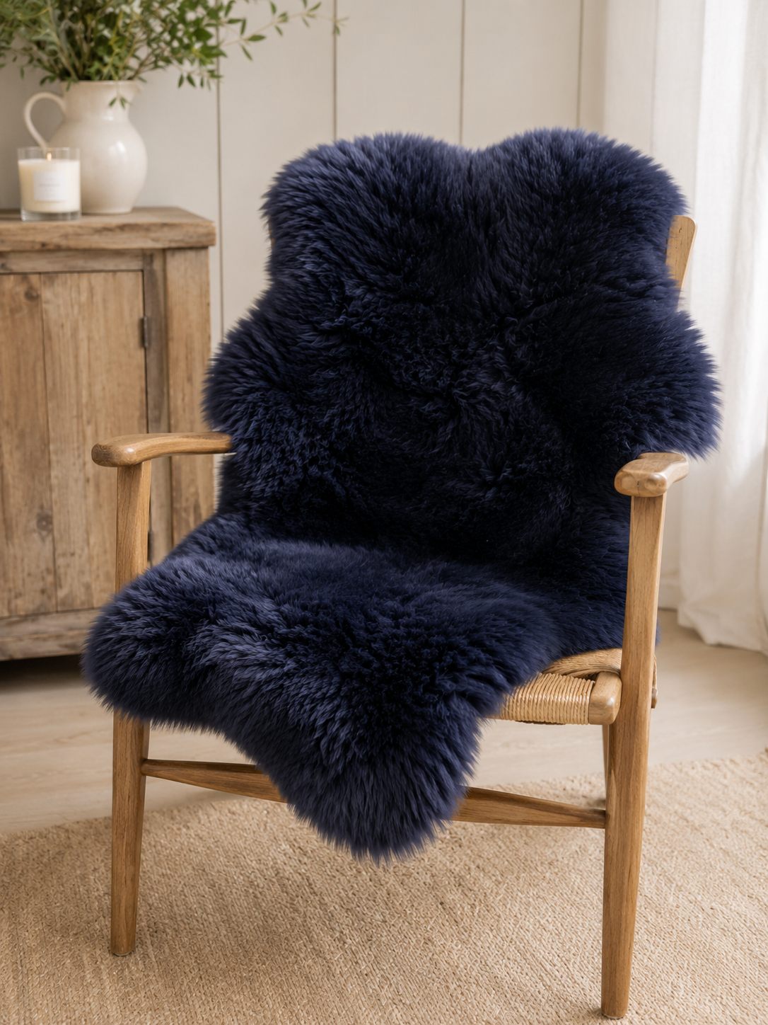 A plush, dark navy blue sheepskin or faux-sheepskin throw blanket draped over a light wood armchair in a bright, neutral-toned room.