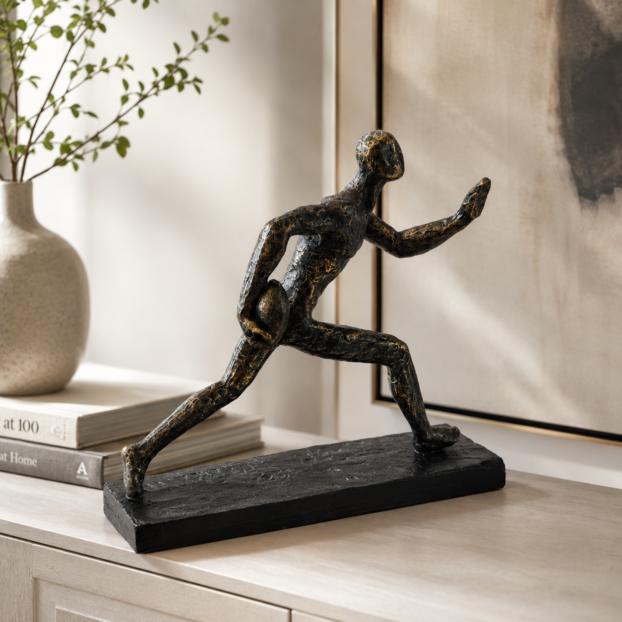 A dark bronze-finished figurative sculpture of a running human form on a rectangular base, displayed on a light wood console table in a styled interior setting.