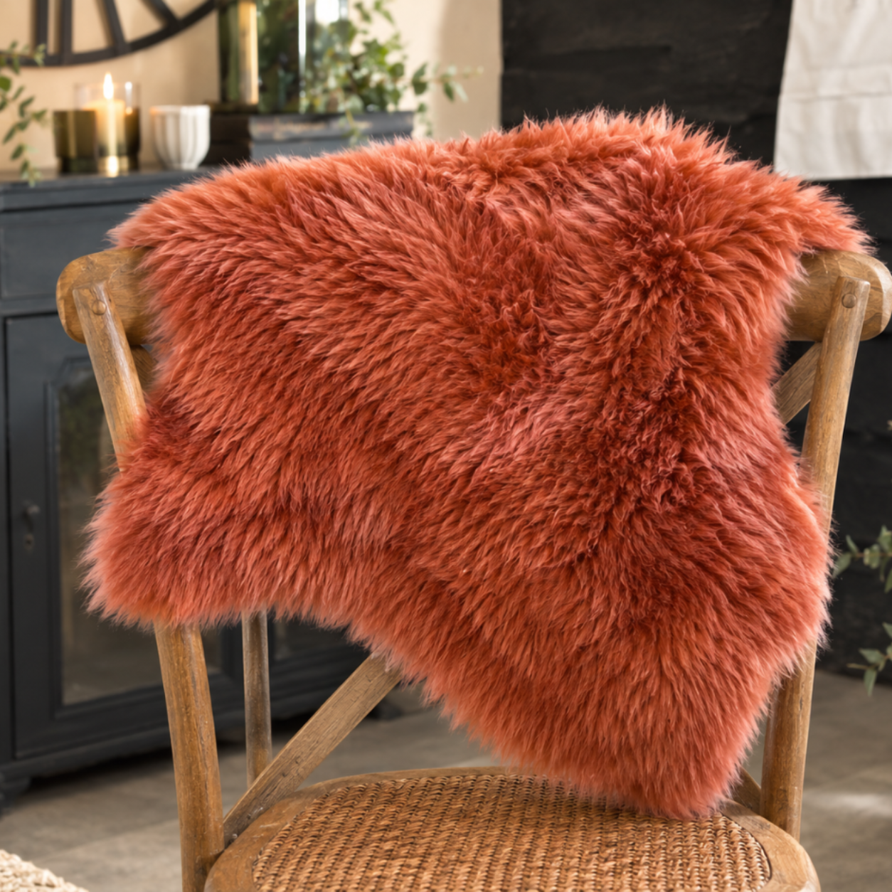 A fluffy faux-fur throw blanket in a warm rust-orange color draped over a wooden chair in a styled interior setting.